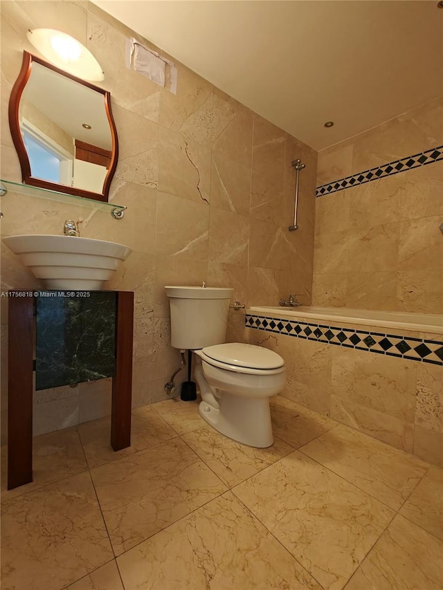 bathroom with toilet, marble finish floor, and tile walls