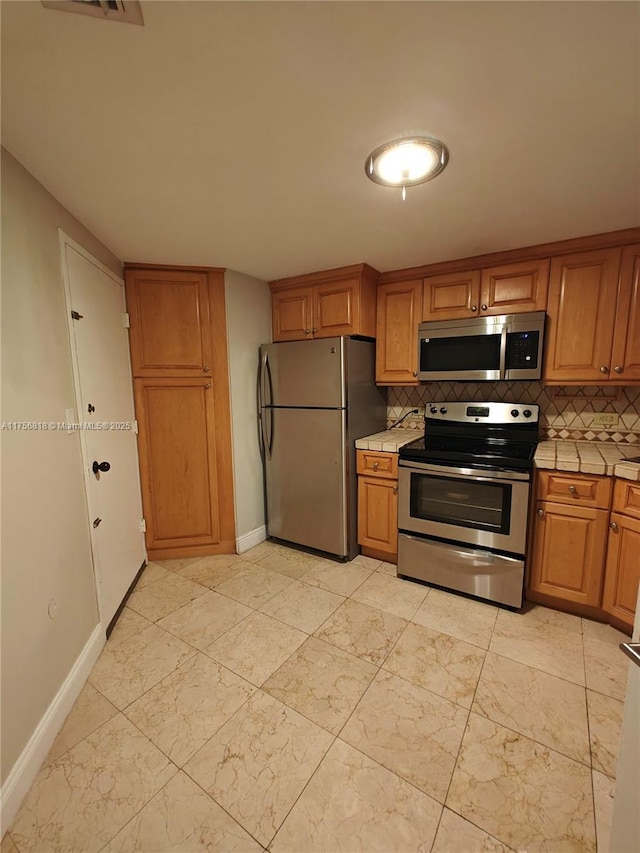 kitchen with stainless steel appliances, tile counters, brown cabinets, and decorative backsplash