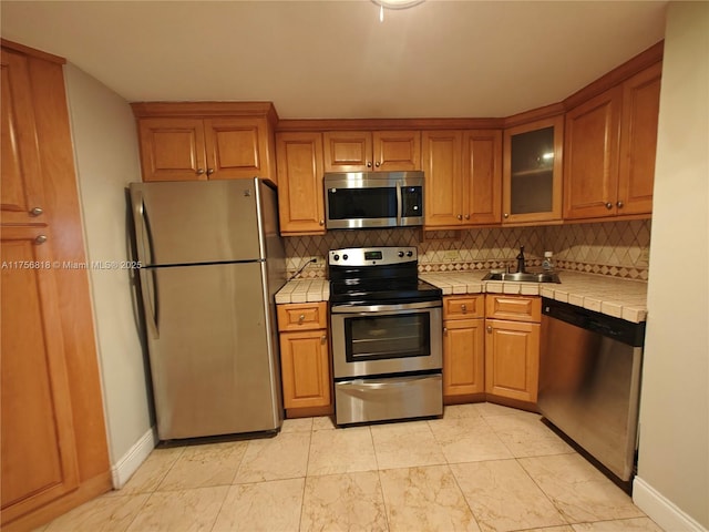 kitchen featuring tile countertops, stainless steel appliances, brown cabinetry, and decorative backsplash