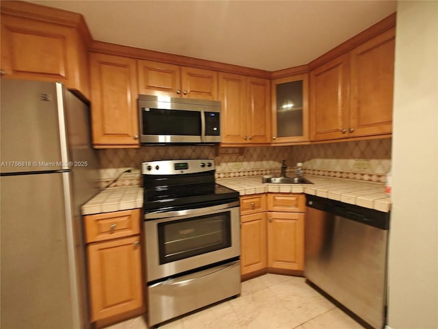 kitchen featuring a sink, appliances with stainless steel finishes, decorative backsplash, and tile counters