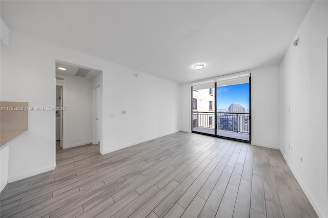 spare room with baseboards, light wood-type flooring, visible vents, and floor to ceiling windows