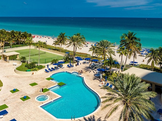 pool with a patio, a beach view, a water view, fence, and a hot tub