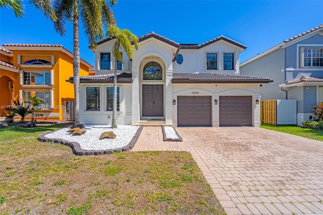 mediterranean / spanish home featuring fence, an attached garage, stucco siding, a tile roof, and decorative driveway