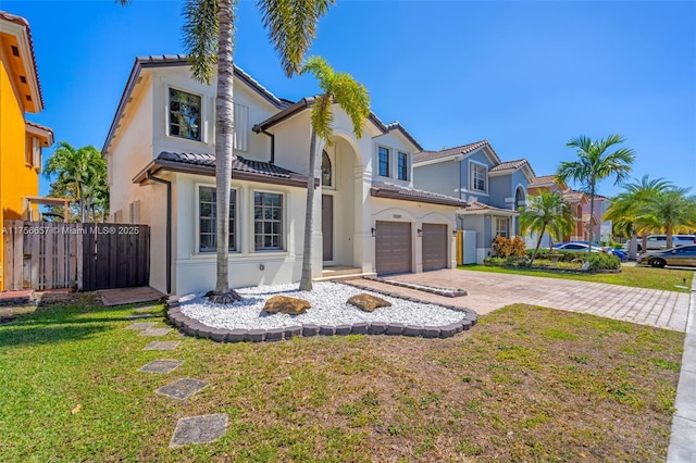 mediterranean / spanish house with a front lawn, fence, stucco siding, decorative driveway, and an attached garage