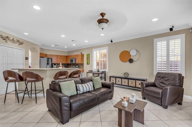 living room featuring baseboards, ornamental molding, light tile patterned floors, recessed lighting, and arched walkways