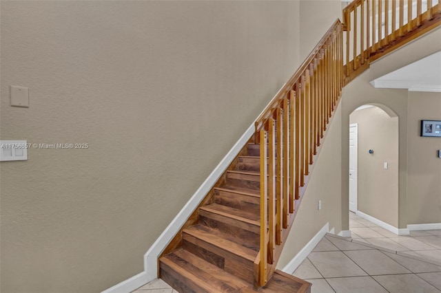 staircase featuring tile patterned flooring, baseboards, arched walkways, and a towering ceiling