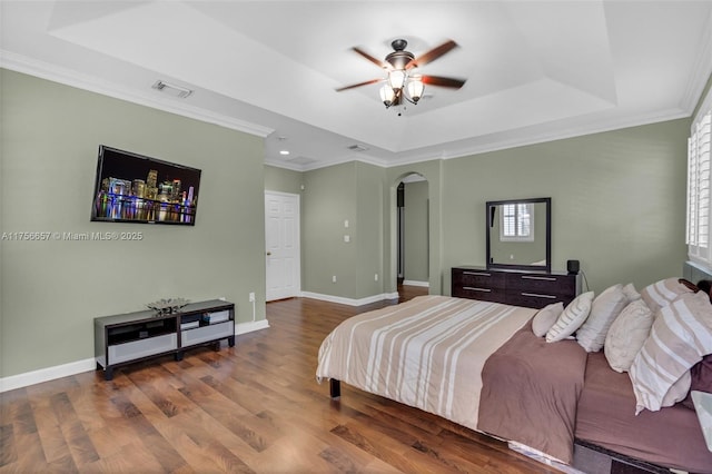 bedroom featuring wood finished floors, visible vents, baseboards, arched walkways, and a raised ceiling