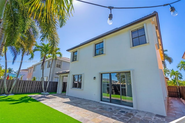 back of property with a fenced backyard, stucco siding, a lawn, and a patio