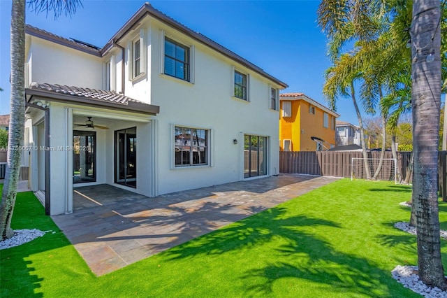 rear view of property with ceiling fan, stucco siding, a yard, a fenced backyard, and a patio