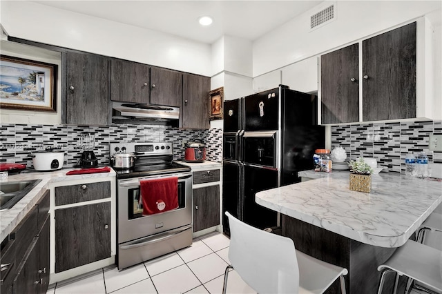 kitchen featuring visible vents, ventilation hood, a breakfast bar, black fridge, and stainless steel range with electric cooktop