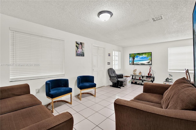 living area featuring light tile patterned flooring, visible vents, and a textured ceiling