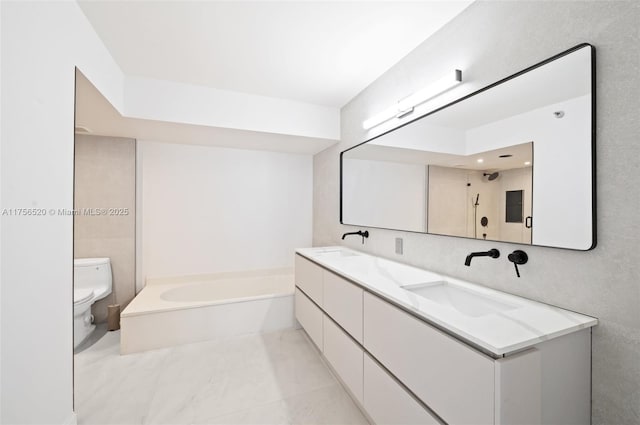 bathroom featuring toilet, a garden tub, double vanity, and a sink