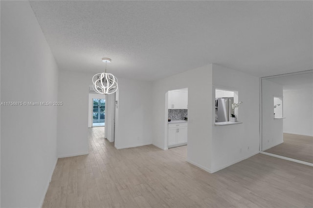 hall featuring light wood finished floors, baseboards, a chandelier, and a textured ceiling