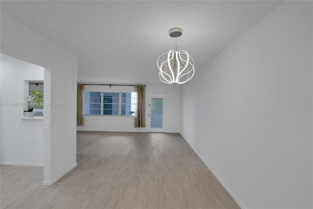 empty room with a chandelier, a textured ceiling, baseboards, and wood finished floors