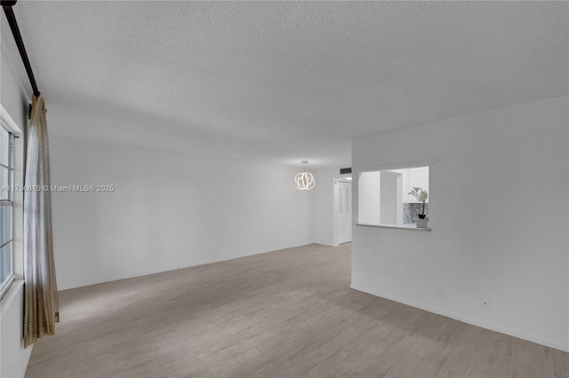 spare room with light wood-style floors, a notable chandelier, and a textured ceiling