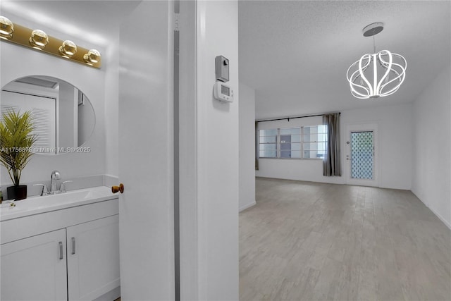 bathroom with a textured ceiling, wood finished floors, vanity, and an inviting chandelier