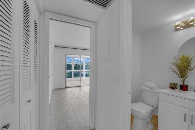 bathroom with visible vents, toilet, wood finished floors, vanity, and a closet