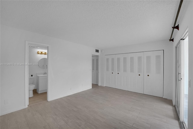 unfurnished bedroom with a textured ceiling, connected bathroom, and light wood-style flooring