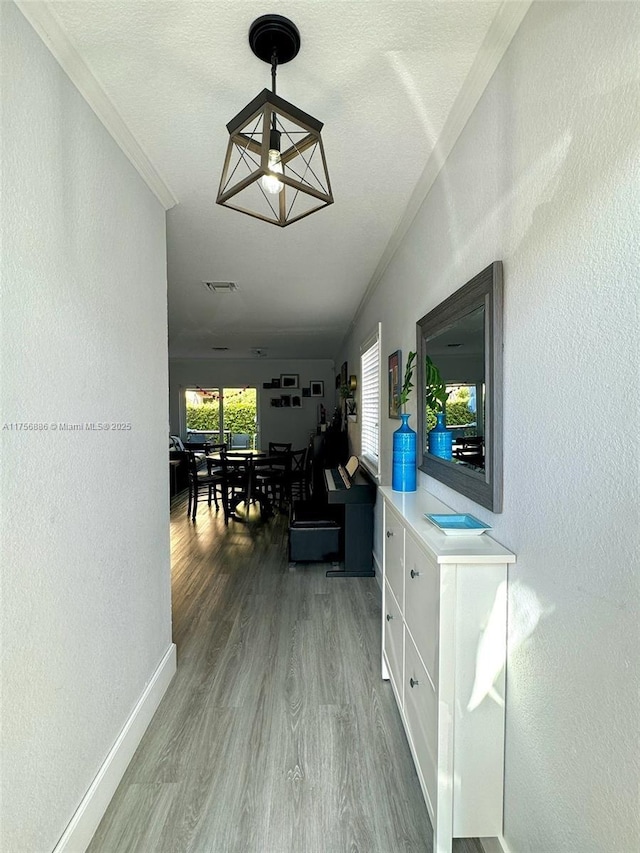 hallway with baseboards, visible vents, wood finished floors, and a textured wall