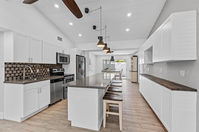 kitchen featuring a breakfast bar area, stainless steel appliances, a kitchen island, a sink, and dark countertops