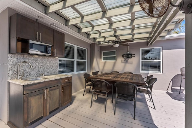 wooden deck featuring outdoor dining area, an outdoor kitchen, a sink, a ceiling fan, and a pergola