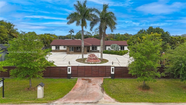 view of front of property featuring stone siding, curved driveway, a front lawn, and a fenced front yard