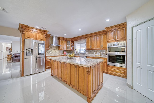 kitchen featuring stainless steel appliances, brown cabinetry, wall chimney exhaust hood, and light tile patterned floors