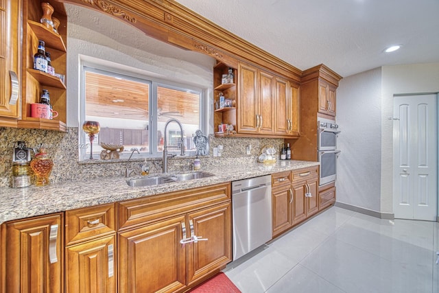 kitchen with brown cabinets, open shelves, stainless steel appliances, a sink, and light stone countertops