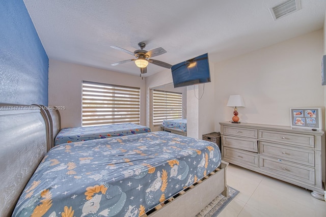 bedroom featuring a textured ceiling, light tile patterned flooring, visible vents, and a ceiling fan