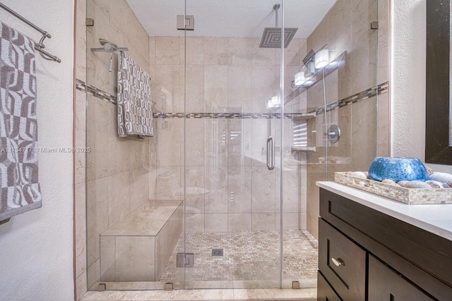 bathroom featuring a textured ceiling, a textured wall, a stall shower, and vanity