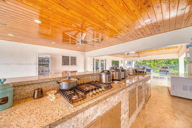 kitchen with a sink, open floor plan, a ceiling fan, stainless steel gas stovetop, and wooden ceiling