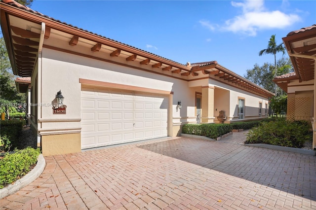 mediterranean / spanish house featuring decorative driveway, an attached garage, a tile roof, and stucco siding