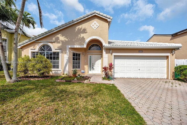 mediterranean / spanish home with a garage, stucco siding, a tiled roof, decorative driveway, and a front yard