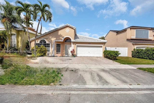 mediterranean / spanish home featuring a garage, a tiled roof, decorative driveway, and stucco siding