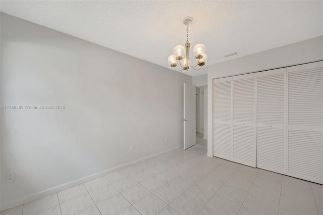 unfurnished bedroom featuring visible vents, light tile patterned flooring, a textured ceiling, a chandelier, and baseboards