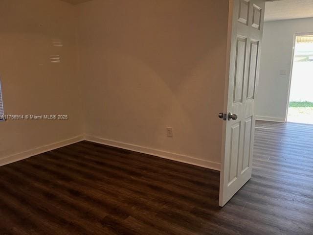 spare room featuring dark wood-style flooring and baseboards