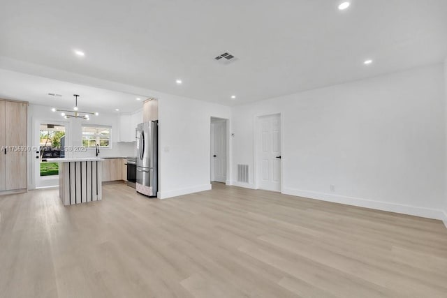 unfurnished living room with light wood-style floors, visible vents, and baseboards