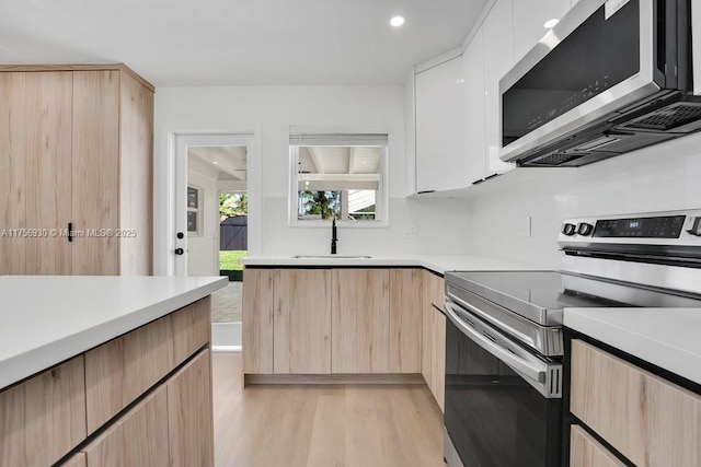 kitchen featuring modern cabinets, appliances with stainless steel finishes, light countertops, light brown cabinetry, and a sink