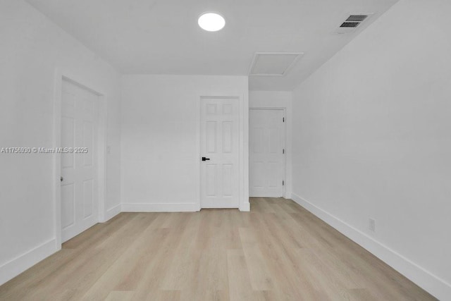 empty room featuring attic access, light wood-type flooring, visible vents, and baseboards