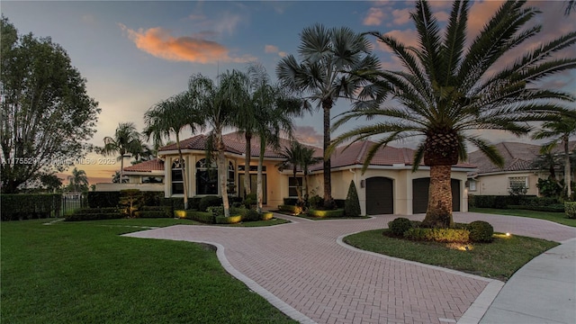 mediterranean / spanish home featuring decorative driveway, a yard, a tiled roof, and stucco siding