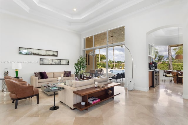 living area featuring a high ceiling, arched walkways, a raised ceiling, and ornamental molding