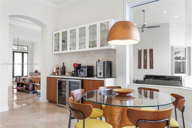 kitchen with tasteful backsplash, brown cabinetry, wine cooler, glass insert cabinets, and ornamental molding