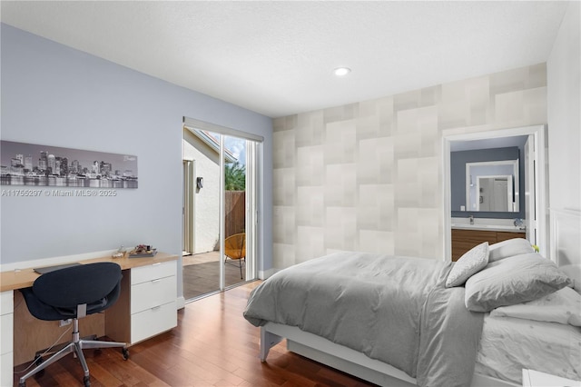 bedroom with built in study area, dark wood-style flooring, ensuite bathroom, access to outside, and recessed lighting