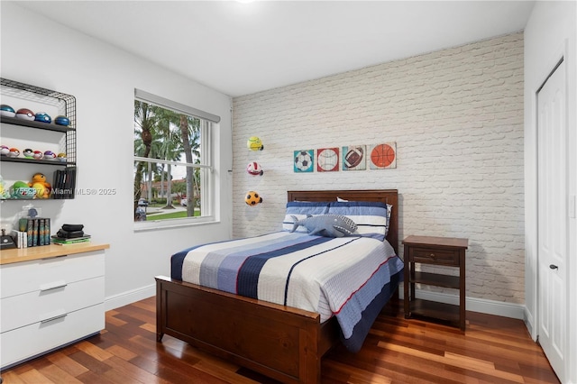 bedroom featuring brick wall, wood finished floors, and baseboards