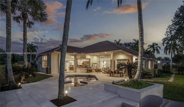 back of house at dusk with a patio and stucco siding