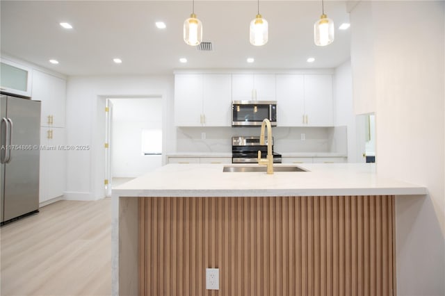 kitchen with pendant lighting, light wood finished floors, stainless steel appliances, visible vents, and a sink