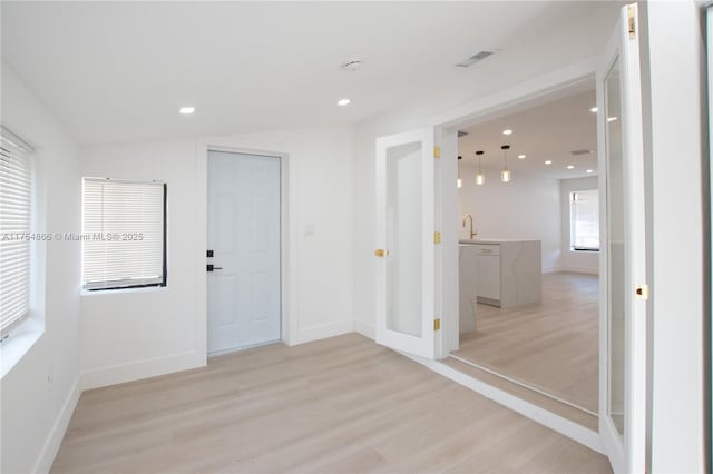 empty room with light wood-style flooring, recessed lighting, a sink, visible vents, and baseboards