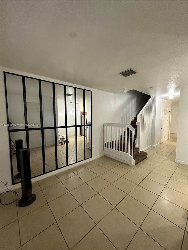 tiled empty room featuring stairs, visible vents, and baseboards