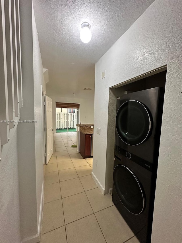 hallway featuring stacked washer and clothes dryer, a textured wall, light tile patterned flooring, a textured ceiling, and baseboards