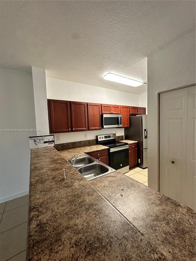 kitchen with light tile patterned floors, stainless steel appliances, a textured wall, a sink, and a textured ceiling